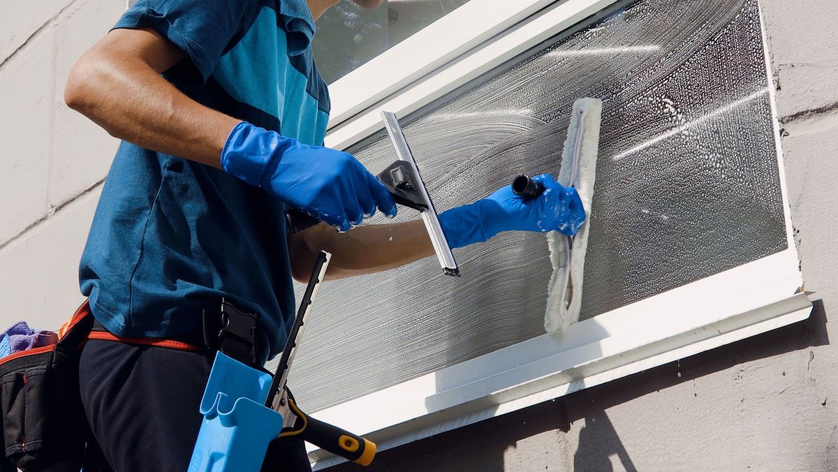 Person mit blauen Putzhandschuhen reinigt eine Fensterscheibe